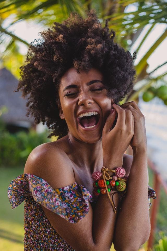 woman with curly hair and glowing skin smiling like crazy - natural black skin care routine
