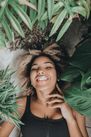 woman smiling surrounded by tropical plants - skincare routine